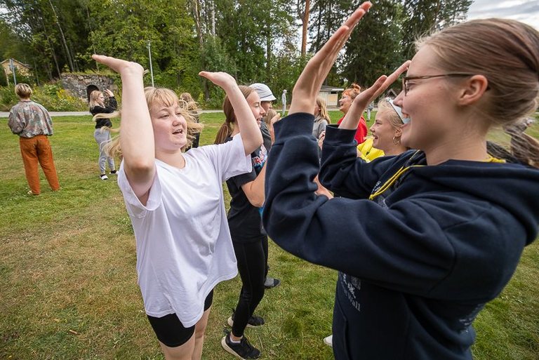 Nuoria rivissä kesäisellä kentällä,jossa he läpsyttävät käsiä yhteen ylhäällä.